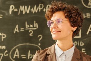 Frau mit Brille vor eine Tafel mit Formeln