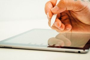 Hand hält einen Ipad-Stift und schreibt auf einem Ipad