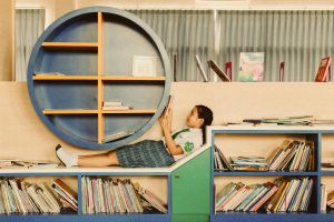 Junges Mädchen liegt auf einem origibell gestalteten Bücherregal.